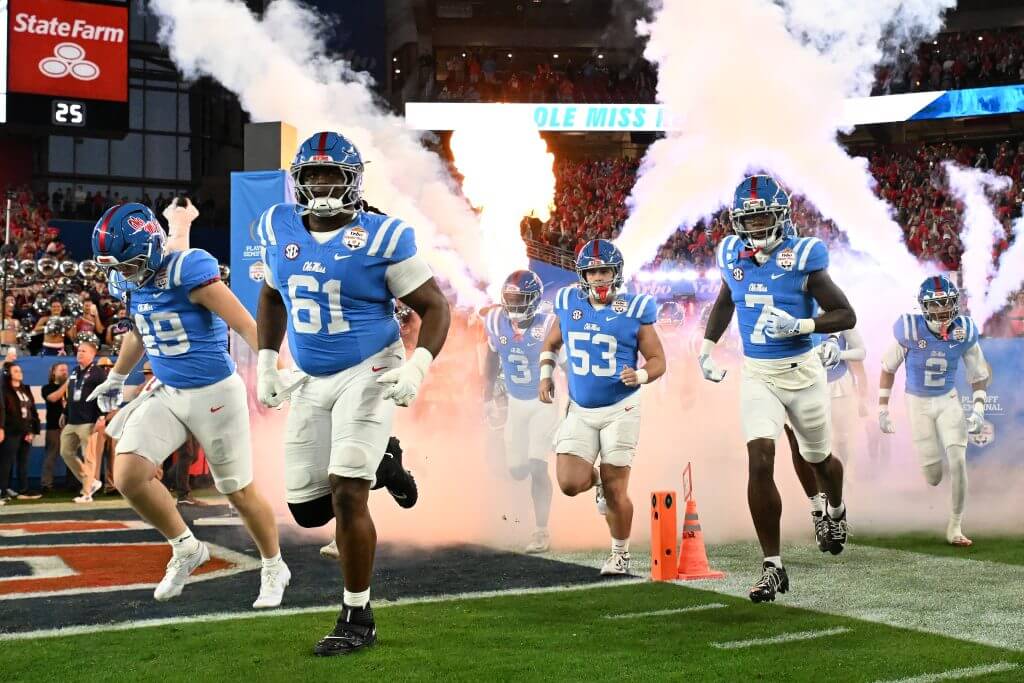 Ole Miss football players run onto the field with smoke behind them