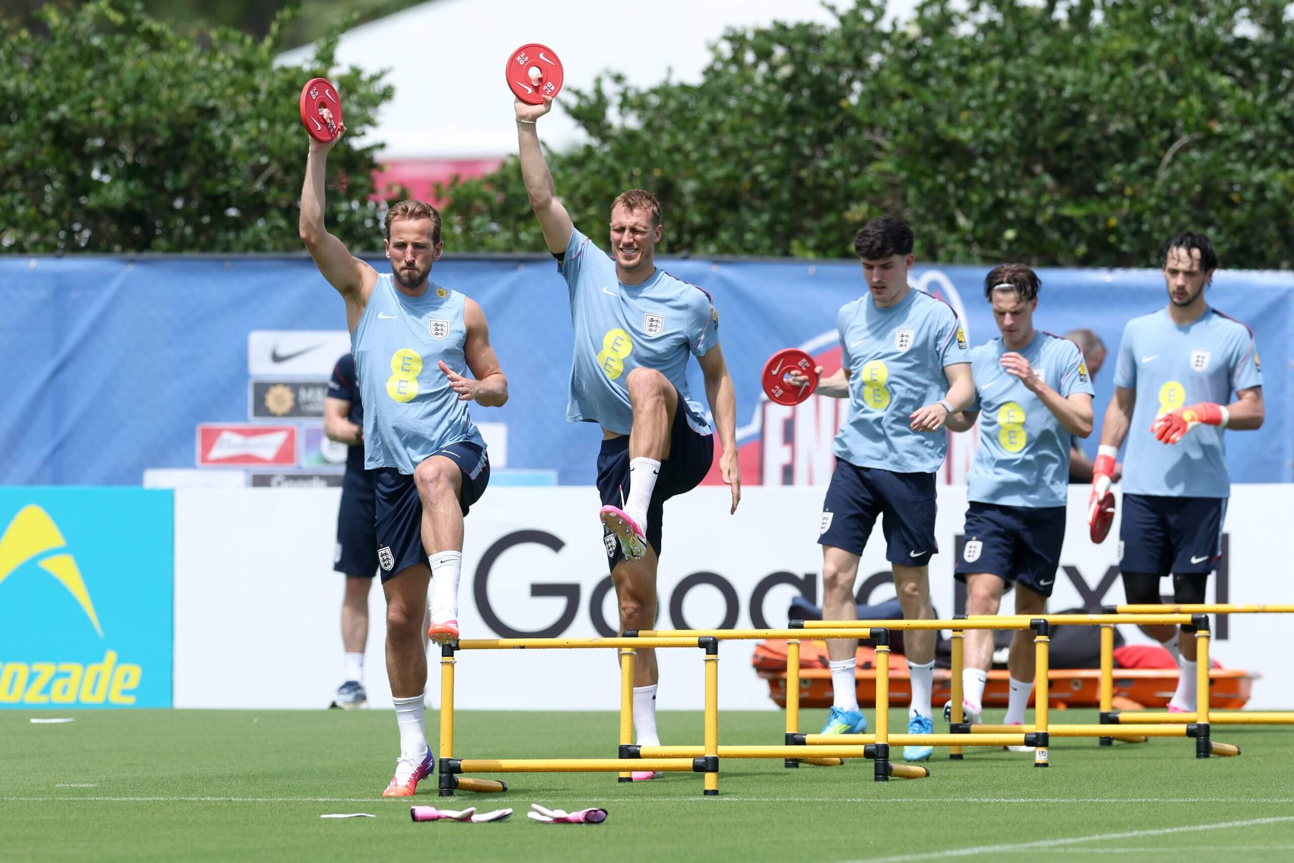 England's Harry Kane and Dan Burn lead a line of players lifting small weights while jogging over hurdles during an England training session