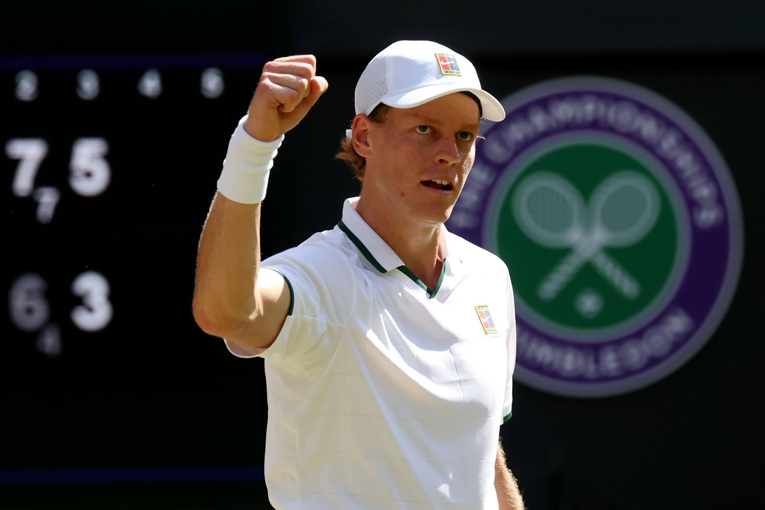 Jannik Sinner pumps his fist in the air in front of the Wimbledon logo.