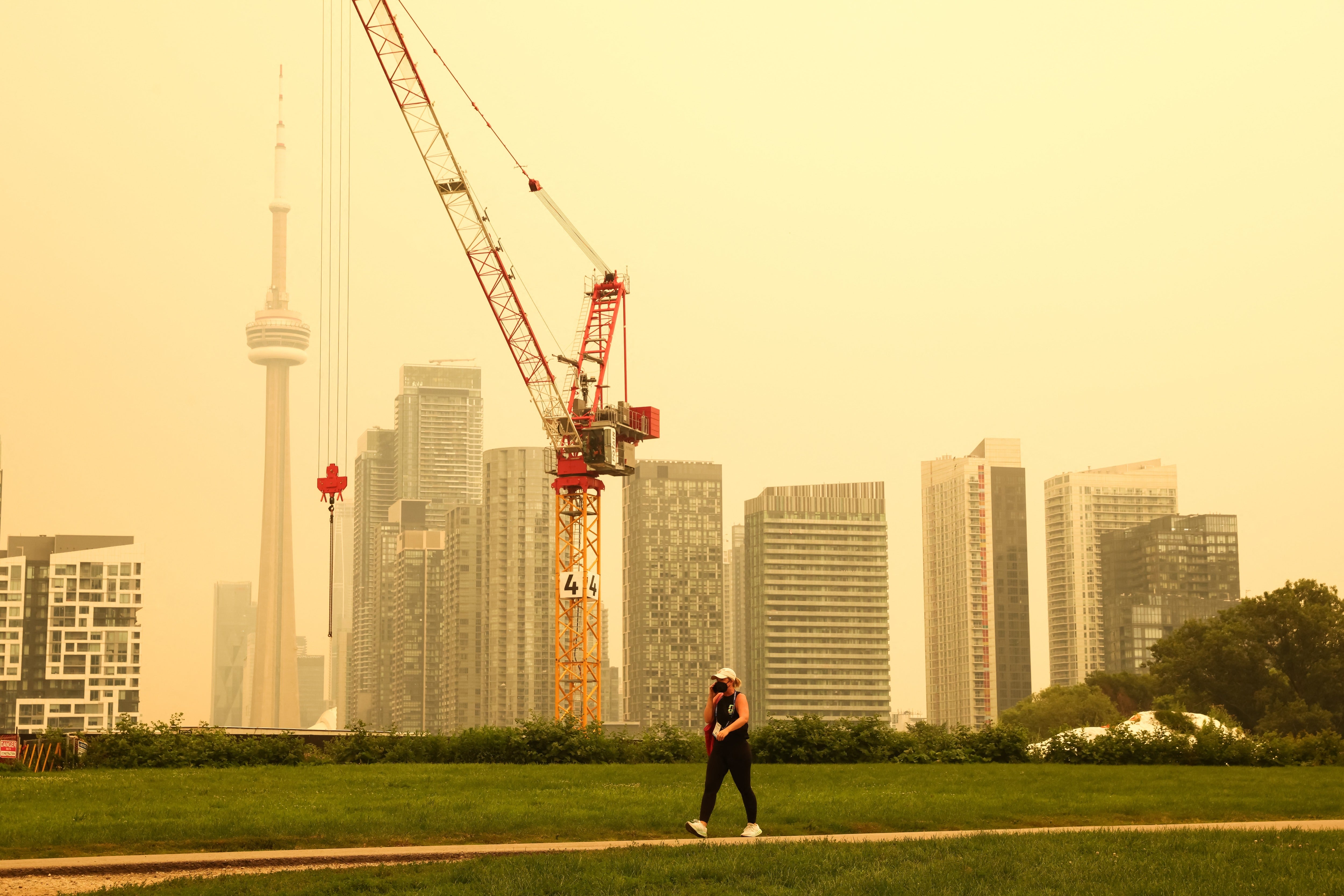 A woman walks by the skyline of downtown Toronto last week amid yellow-hued smoke. More than 900 wildfires are burning across a wide swath of Canada
