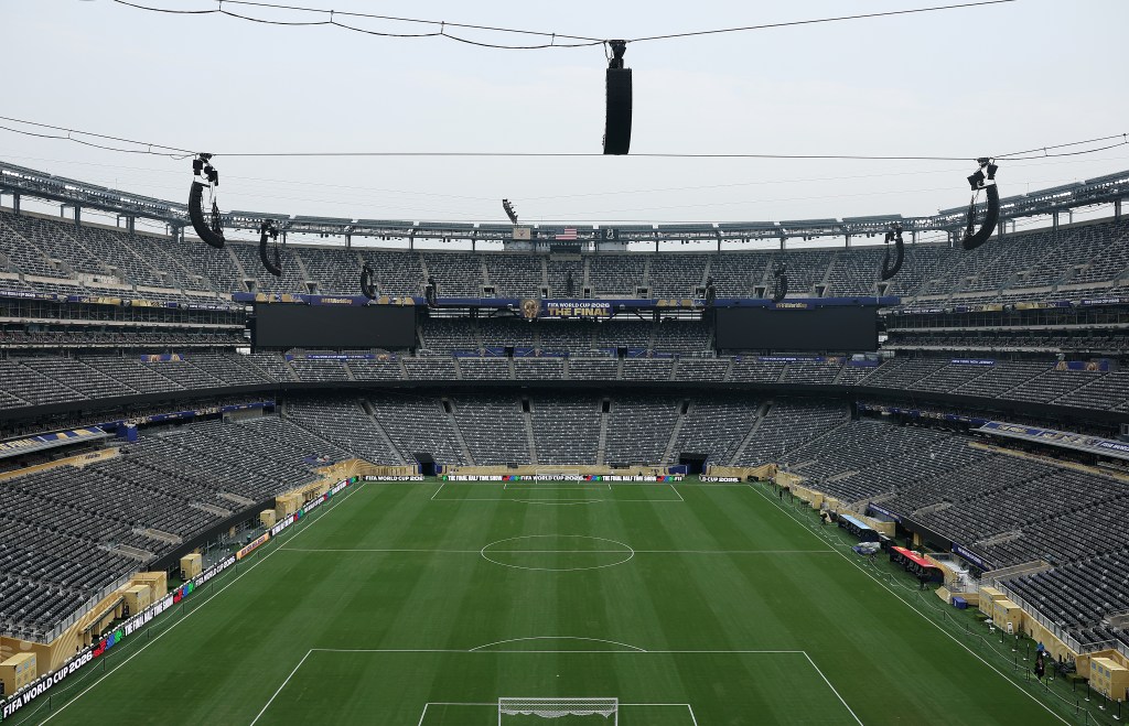 An empty football stadium with green grass field, black seating, and "FIFA WORLD CUP 2026 THE FINAL" banners.