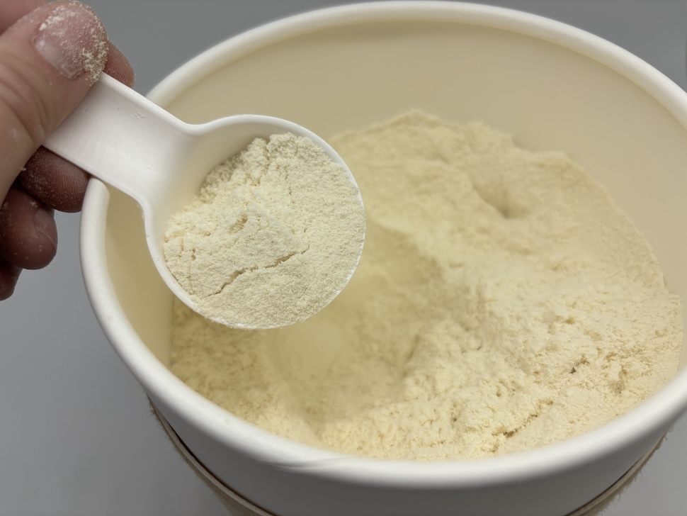 An open canister of Heart & Soil Animal-Base Protein. A hand is scooping out some of the off-white powder.