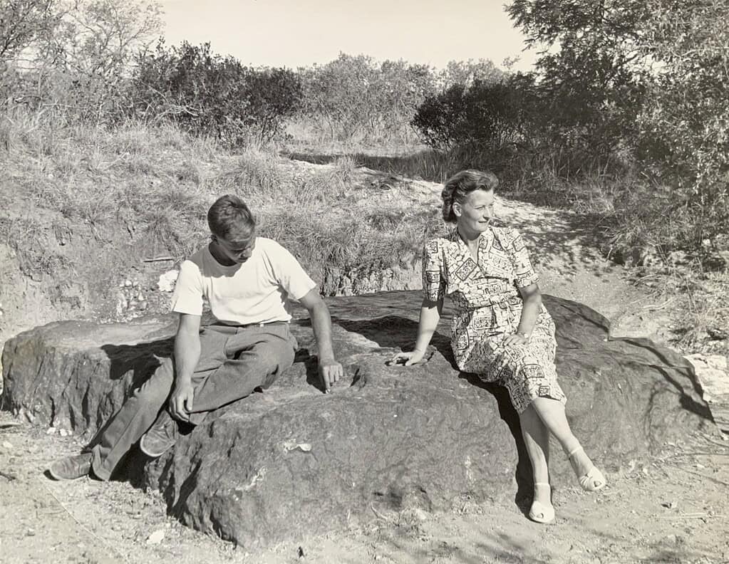 Man and woman relaxing on a rock in a natural setting, vintage black-and-white photo.