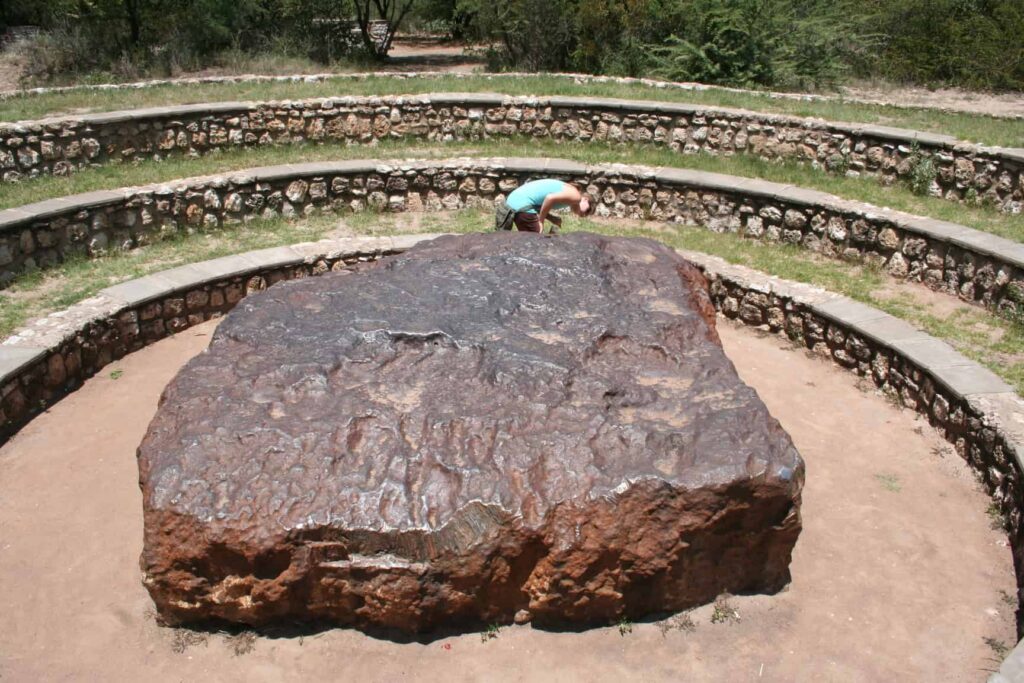 Large ancient stone in open-air archaeological site with tiered seating.