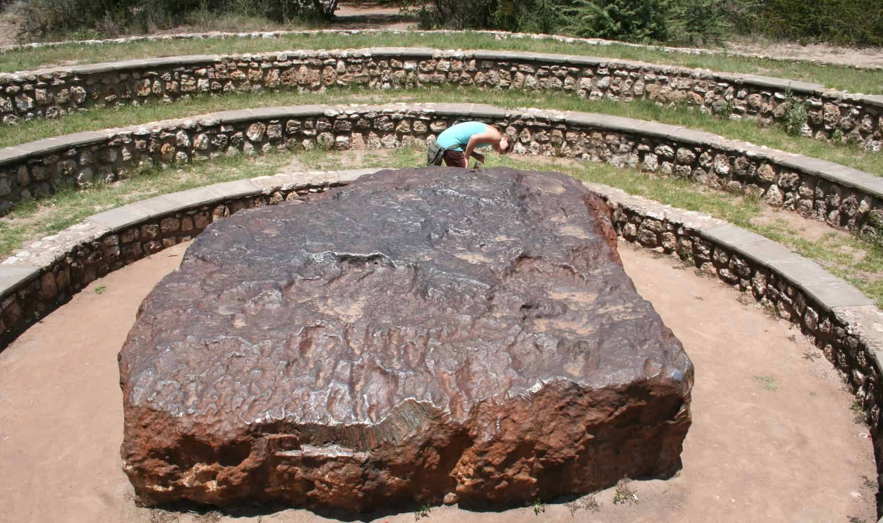 Large ancient stone in open-air archaeological site with tiered seating.