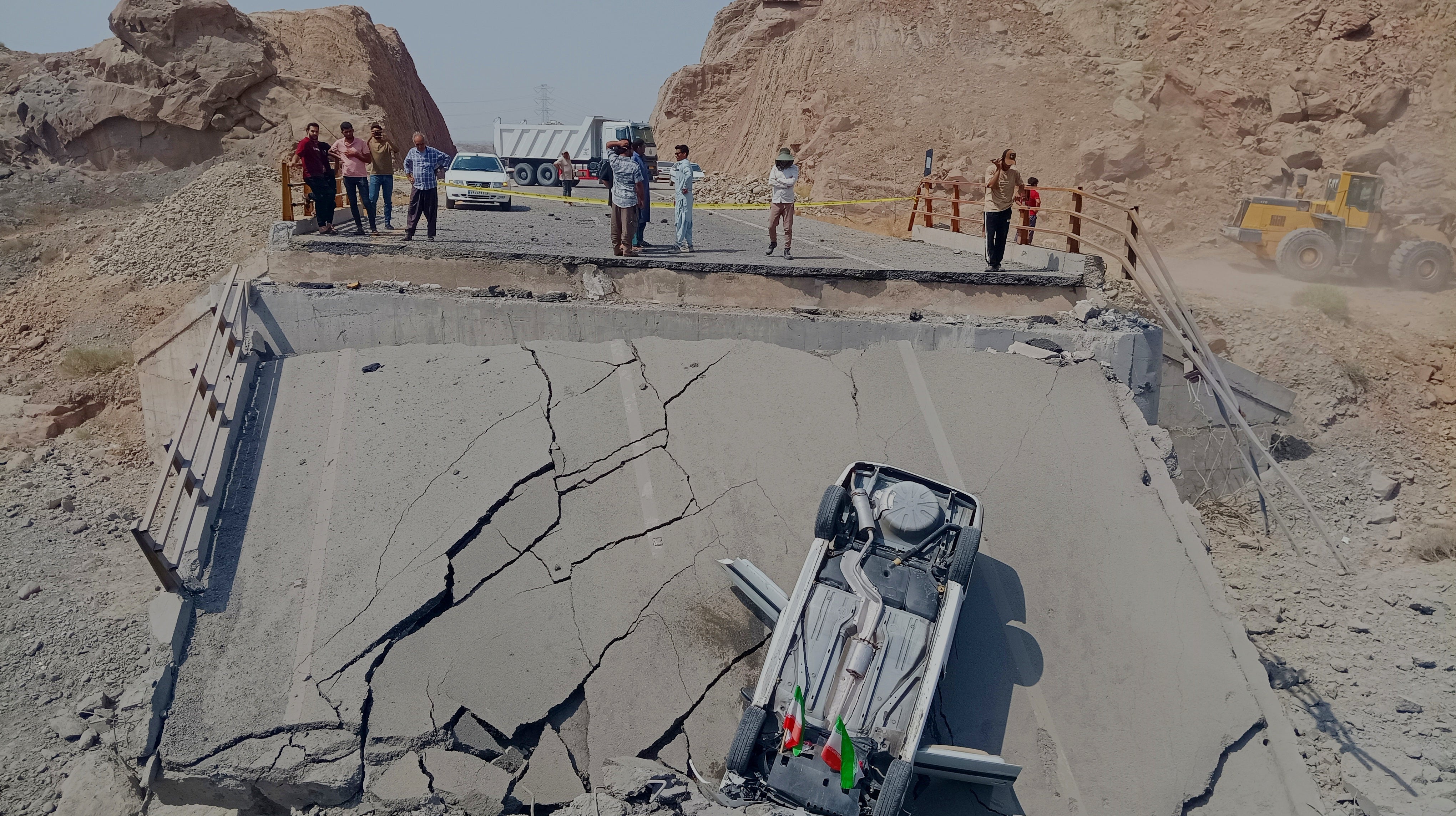 An overturned car sits on a section of a destroyed bridge after a strike in Hormozgan province