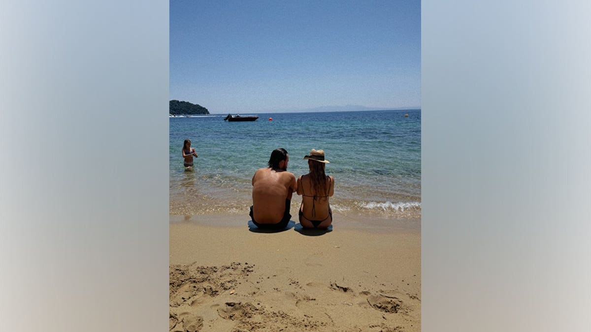 Kate Hudson and fiancé Danny Fujikawa sit side by side on the beach while looking out at the ocean during a family vacation in Greece.