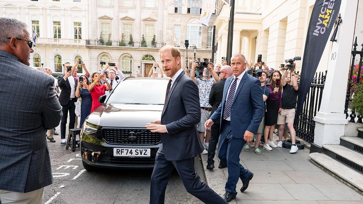 Prince Harry in a dark suit being photographed outside in London.
