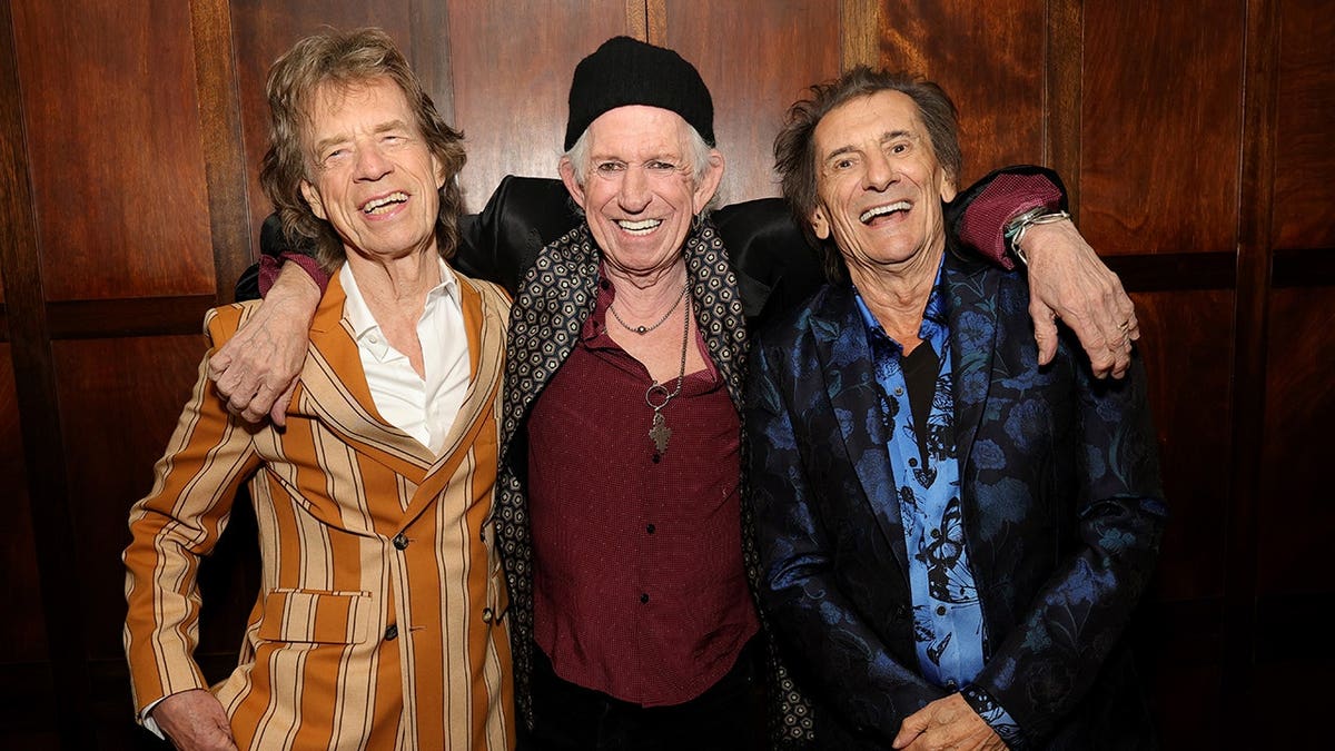 Mick Jagger, Keith Richards and Ronnie Wood embracing each other in Brooklyn and smiling.