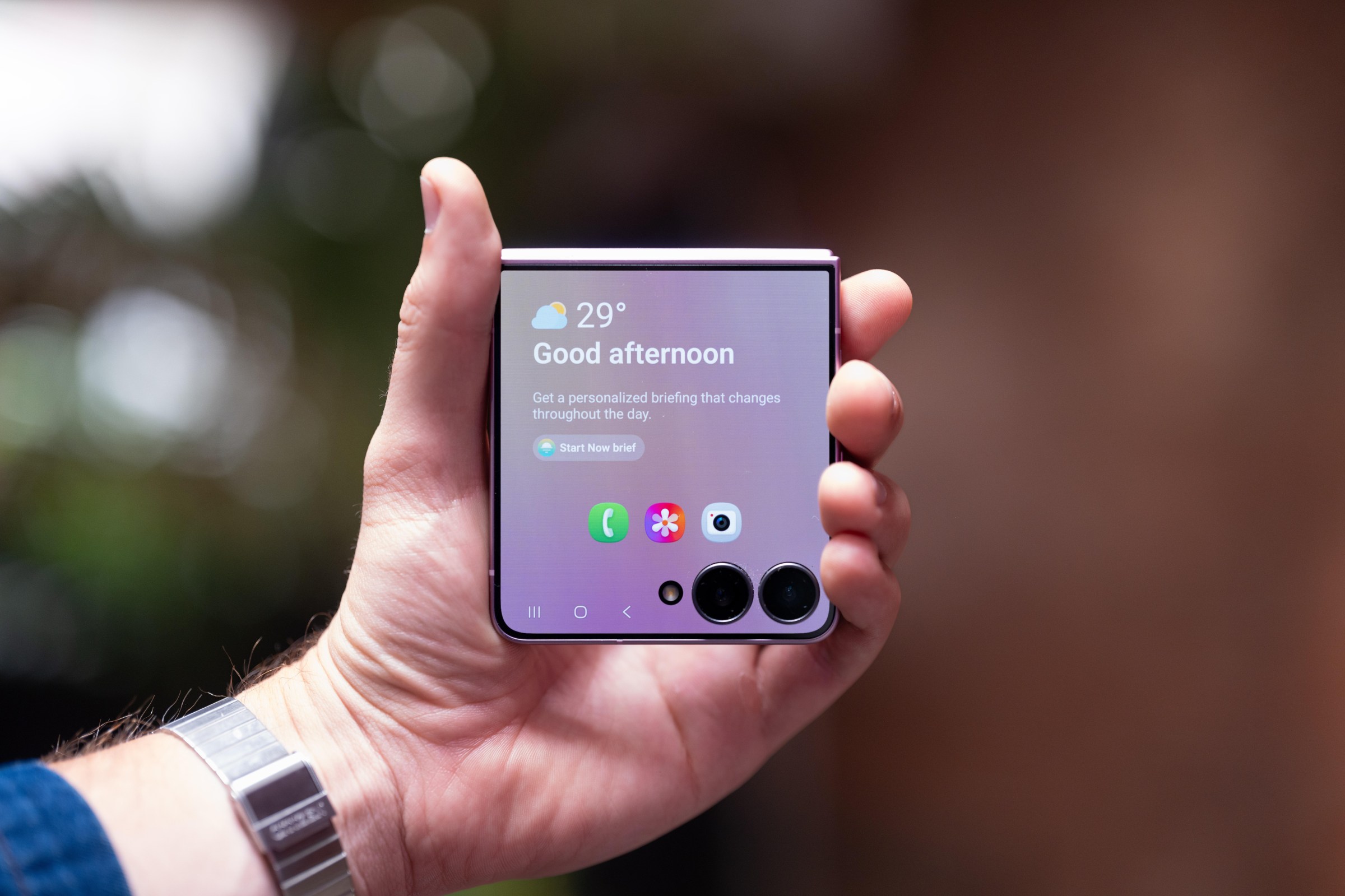 A hand holding a closed Samsung Galaxy Flip 8, with the front screen on