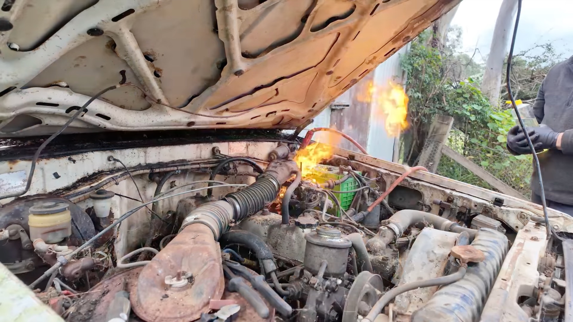 Flames shoot out of the carburetor of a derelict Toyota Land Cruiser