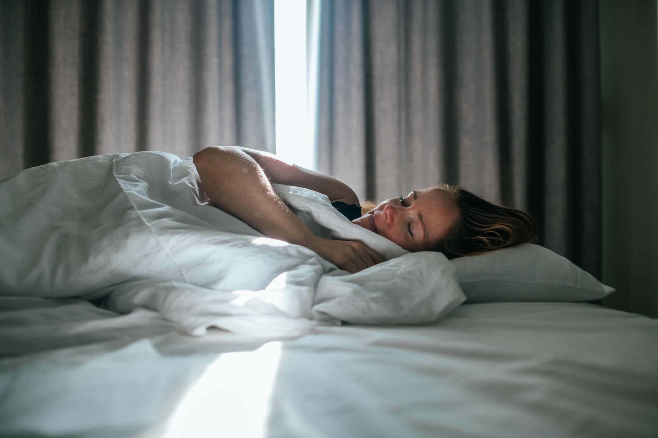 Woman sleeping well in a nice sleeping room. Sunny daylight is coming through the curtains in the back.