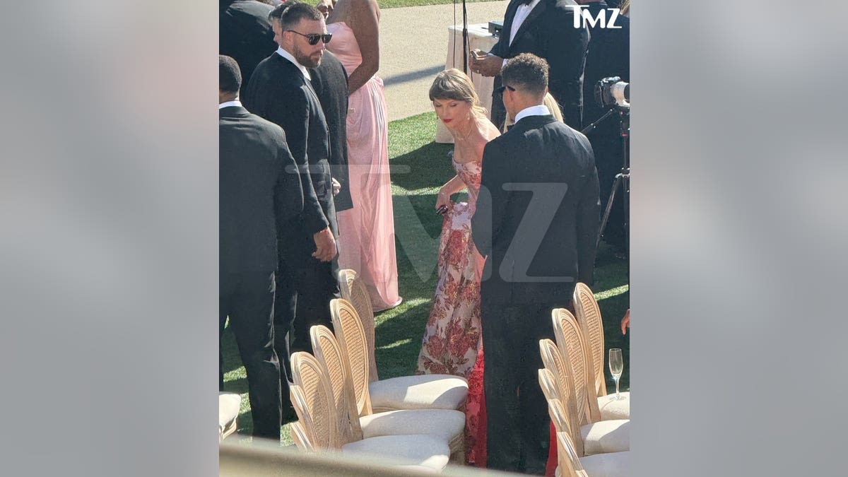 Taylor Swift stands outside in a floral brocade dress
