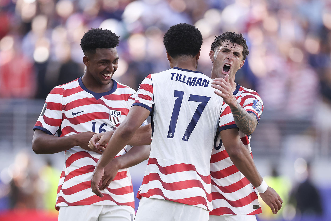 Three U.S. players celebrating on the field, one shouting with arms raised, another smiling and reaching toward him.