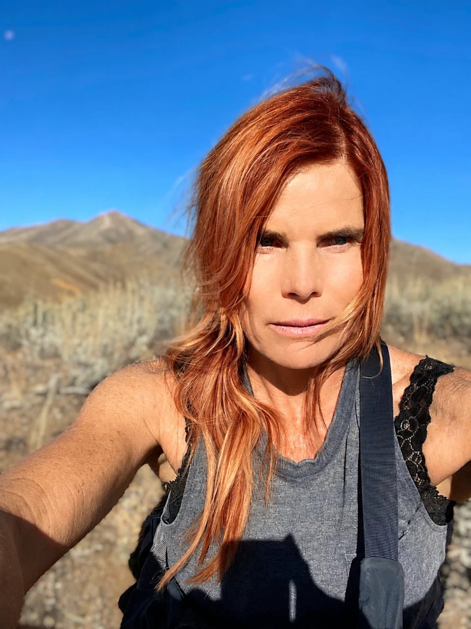 Mariel Hemingway takes a makeup-free selfie during a mountain hike, with sagebrush hills and peaks behind her.