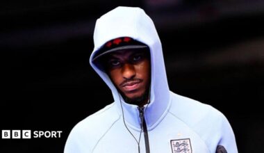 Marcus Rashford wearing a white England zip-up top, hood pulled up over his head