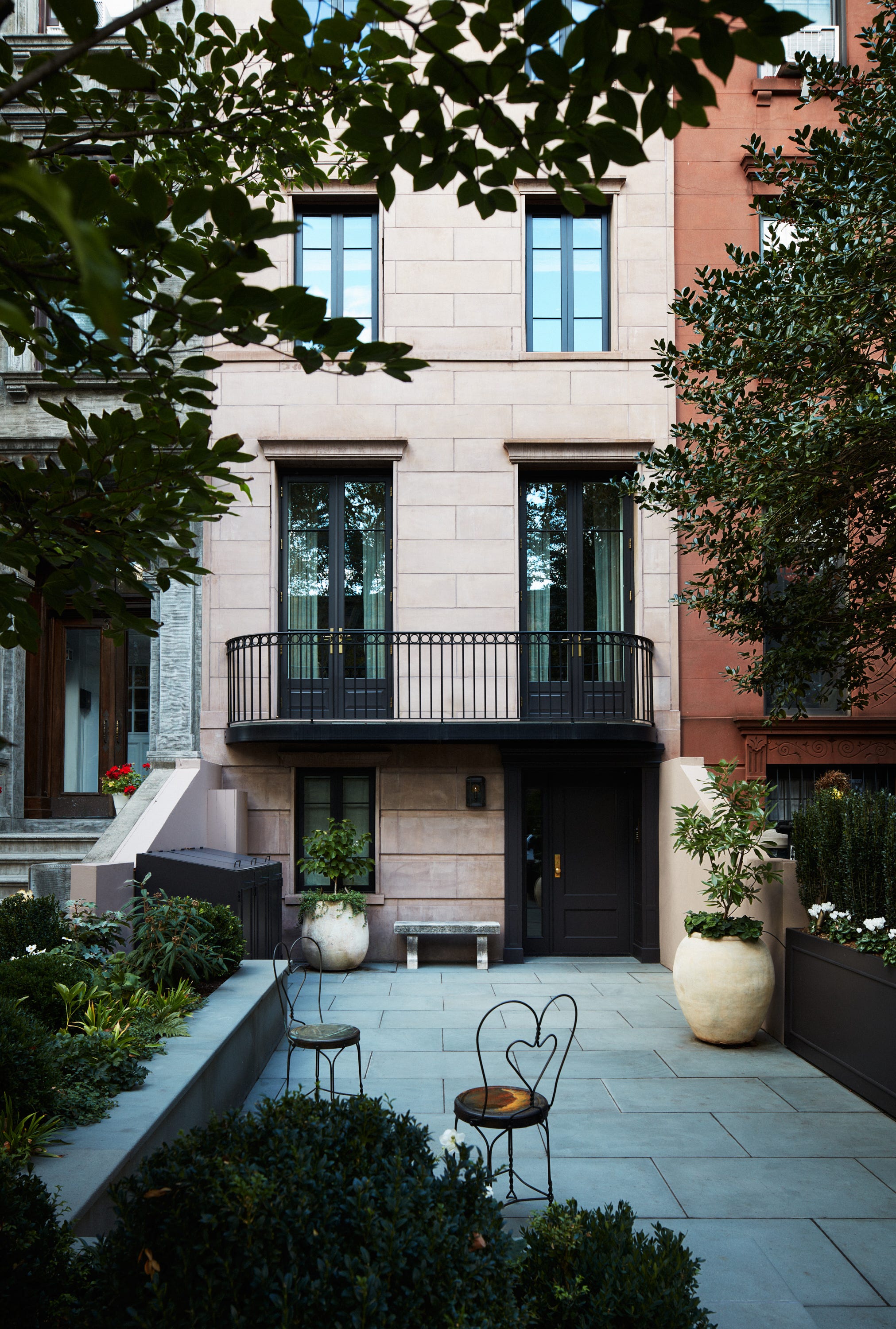 Elegant courtyard featuring a modern building facade, planters, and outdoor seating surrounded by greenery.