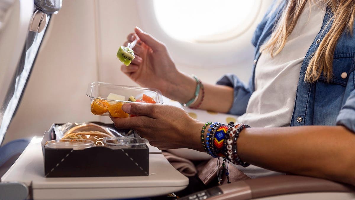 A woman eats fruit on an airplane.