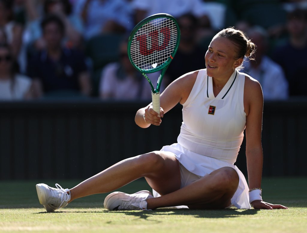 Amanda Anisimova sitting on the court with a tennis racket in hand during a Wimbledon match.