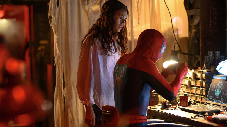 Zendaya as MJ standing by a desk and watching Tom Holland as Peter Parker in his superhero suit in Spider-Man: Brand New Day