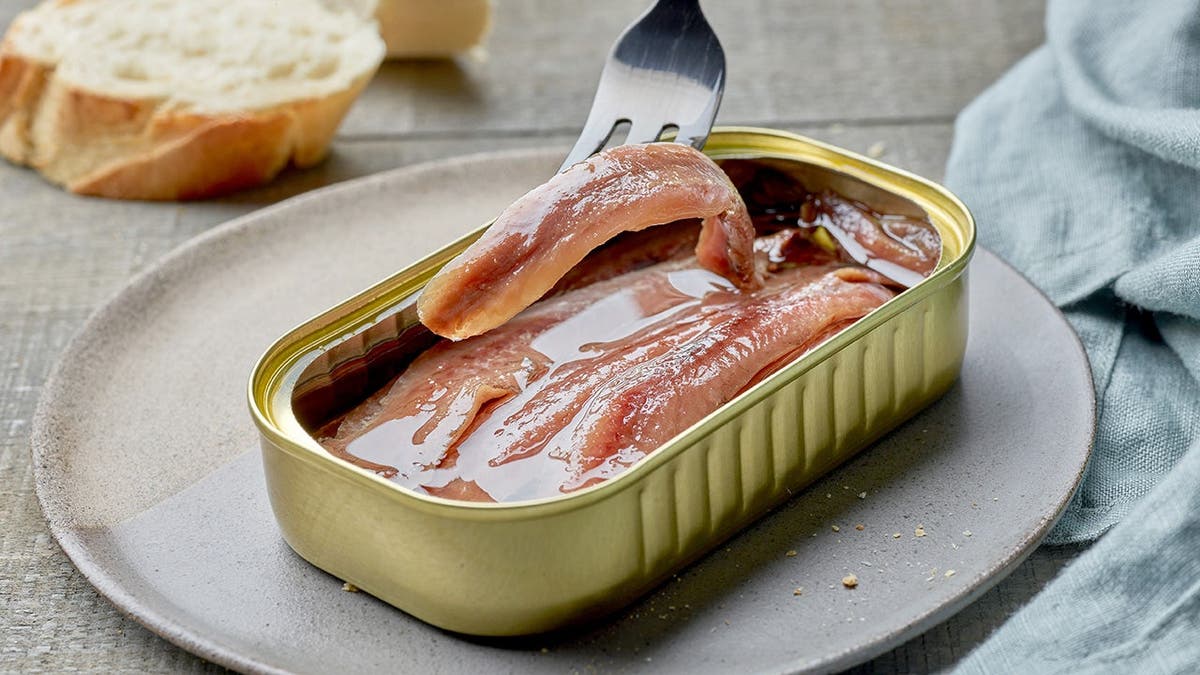 Rows of salted anchovy fillets packed tightly in oil inside an open tin.