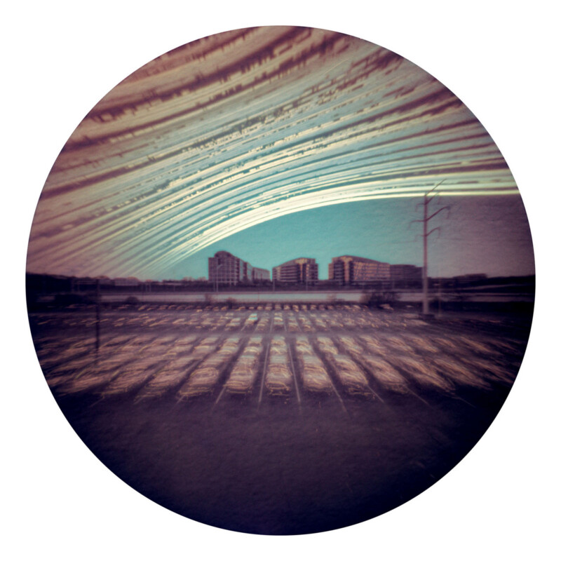 A circular photo shows a cityscape with streaks of light arcing across the sky above buildings and parked cars, captured with a long-exposure technique, creating surreal, sweeping patterns.