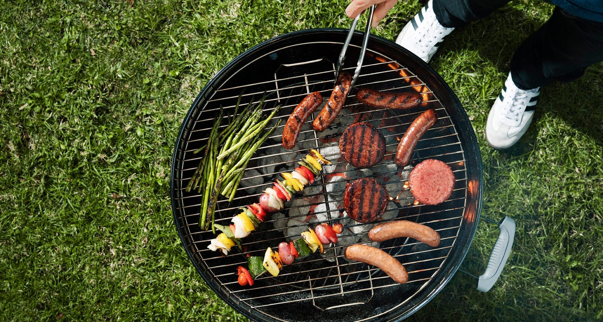 A man uses tongs to rotate food on a grill.