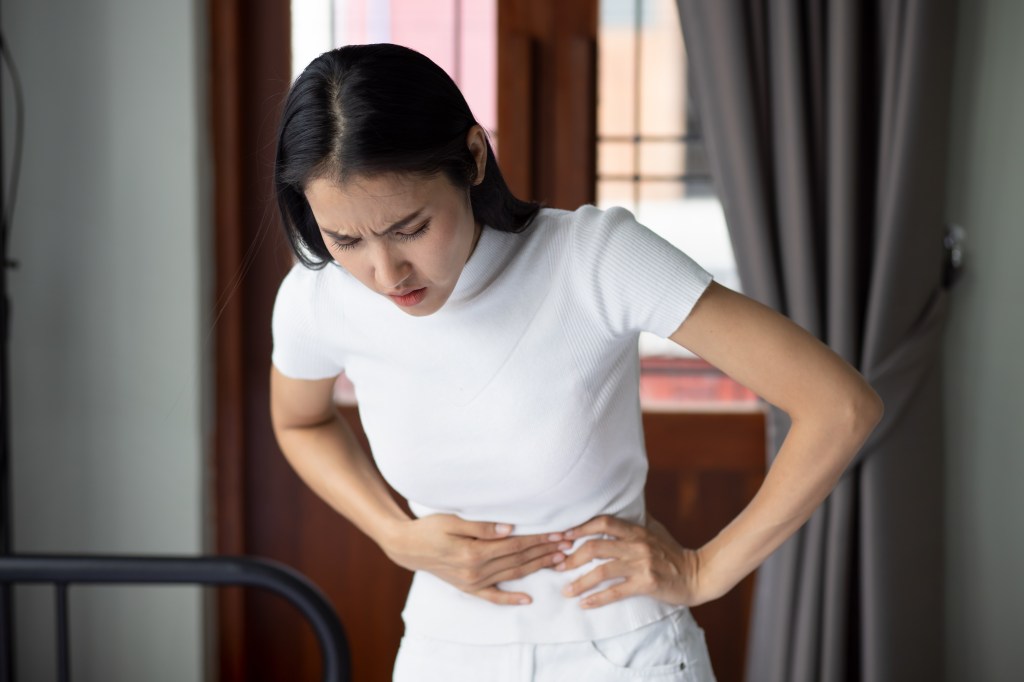 Asian woman clutching her stomach in pain.