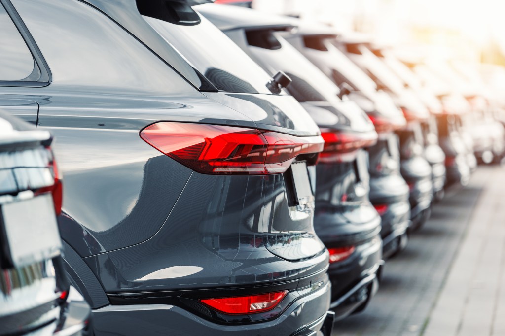 Rear view of a fleet of new grey SUV cars parked in a row at a dealership lot.