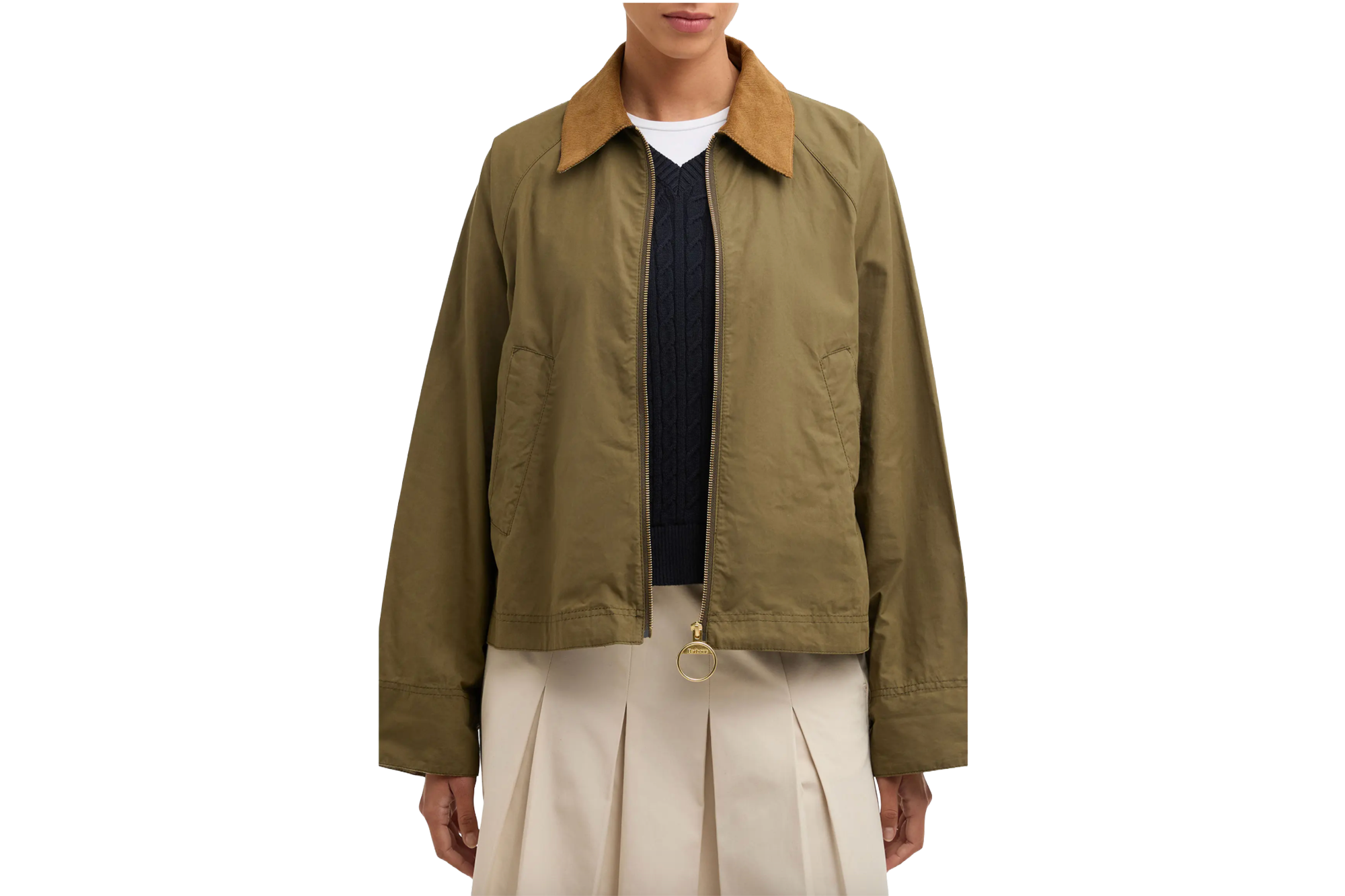 A person wearing a cropped olive Barbour jacket with a brown corduroy collar over a navy blue sweater and cream pleated skirt.