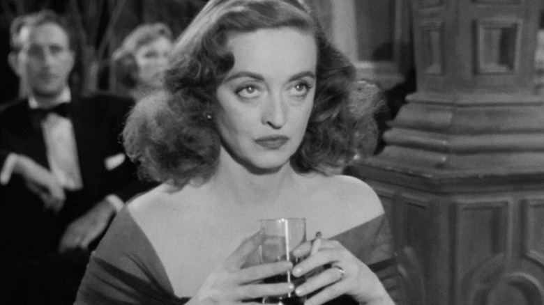 Bette Davis glares upwards with a drink and cigarette in hand as Margo Channing in All About Eve