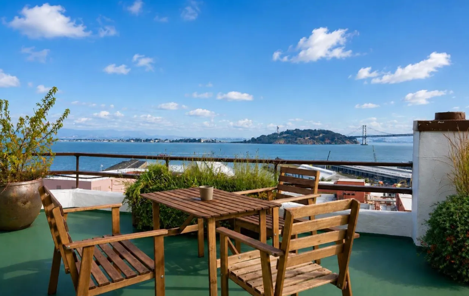 Rooftop terrace with wooden furniture and a scenic view of the bay and distant bridge. Rooftop terrace with wooden furniture and a scenic view of the bay and distant bridge.