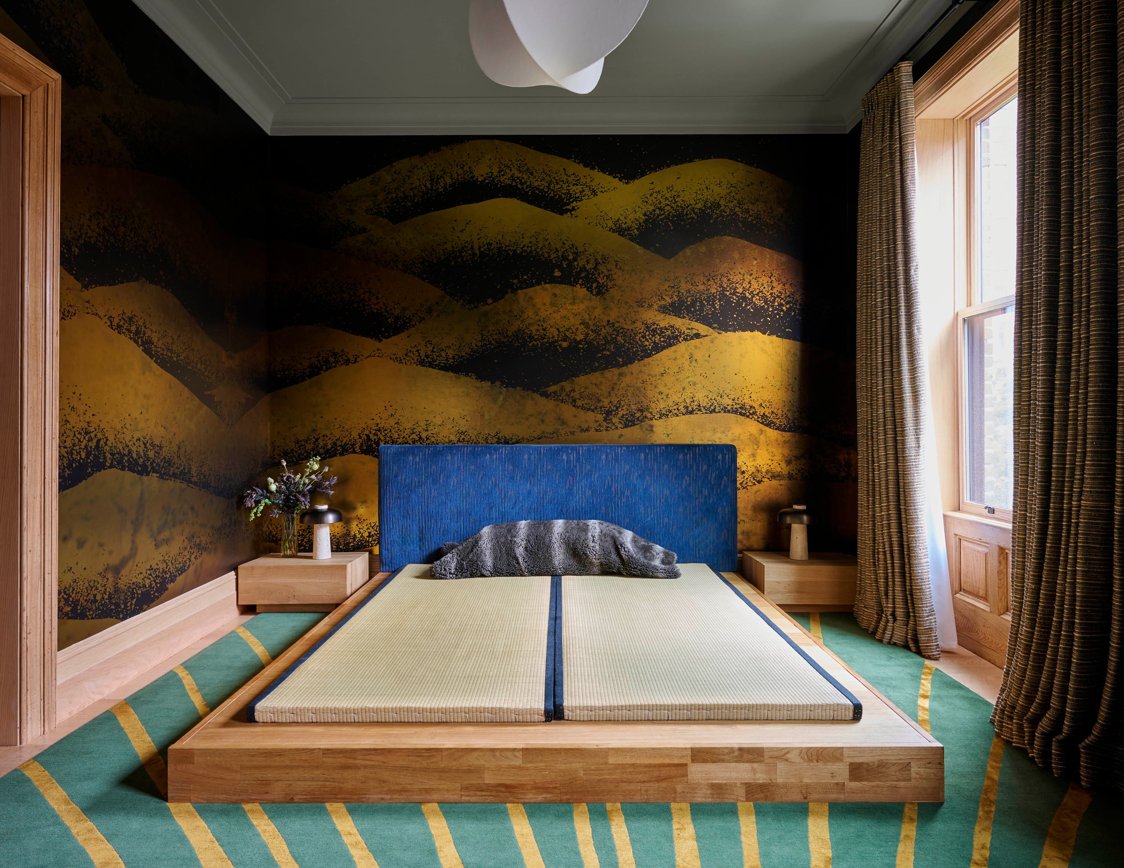 A modern bedroom featuring a tatami mat, blue bed frame, patterned walls, and natural light from a window.