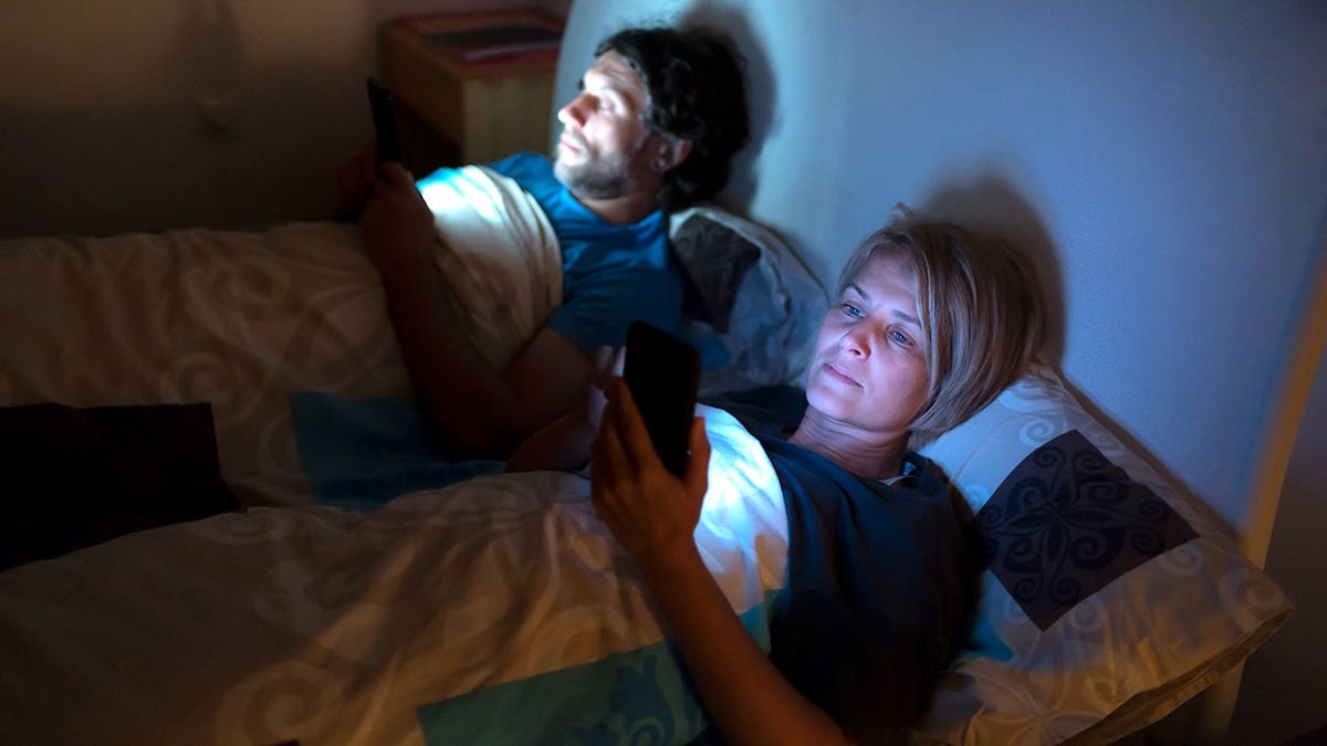 Couple checks a phone while in bed before sleep.