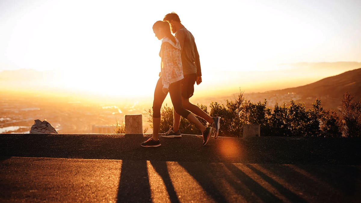 Couple walk along road at sunrise. Couple talking a walk on hillside road with bright sunlight.