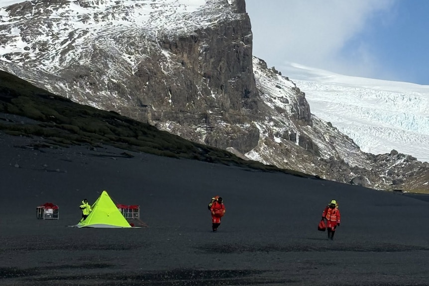 A tent and expeditioners on a desolate island with snow covered peak nearby.