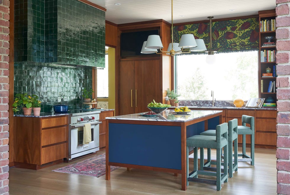Modern kitchen with green tile backsplash, wooden cabinets, marble countertop, and seating at an island with fruit display.