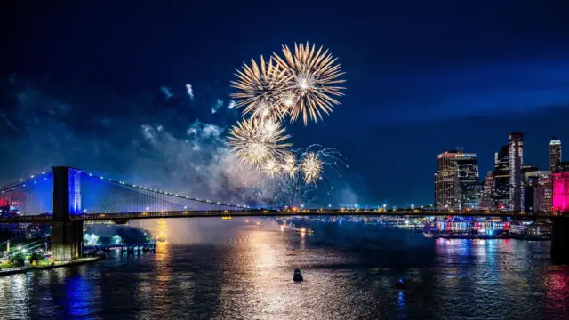 Fireworks light up di sky ova di Brooklyn Bridge during one fireworks display wey mark di 250th anniversary of US independence for New York, New York