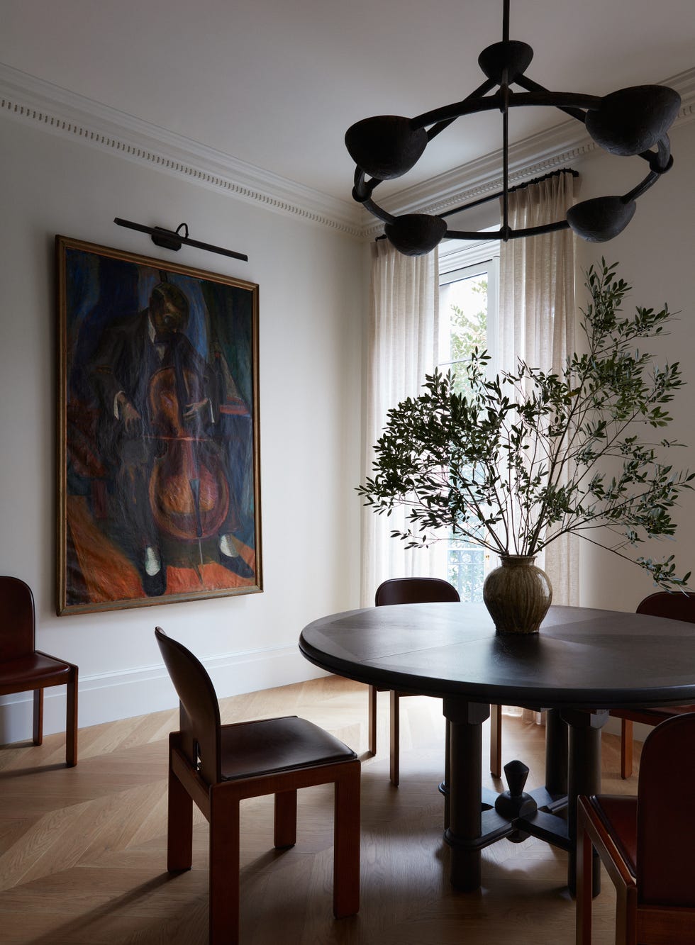 Dining room featuring a round table, chairs, a vase with branches, and an art piece depicting a musician.