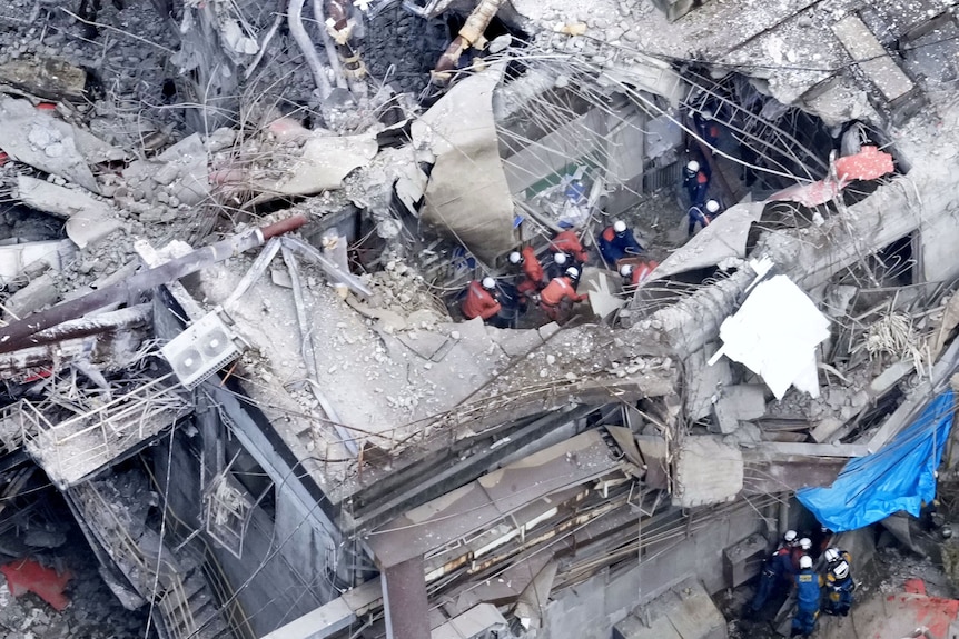 An aerial photo of half a dozen orange-clothed rescue workers among grey building rubble.