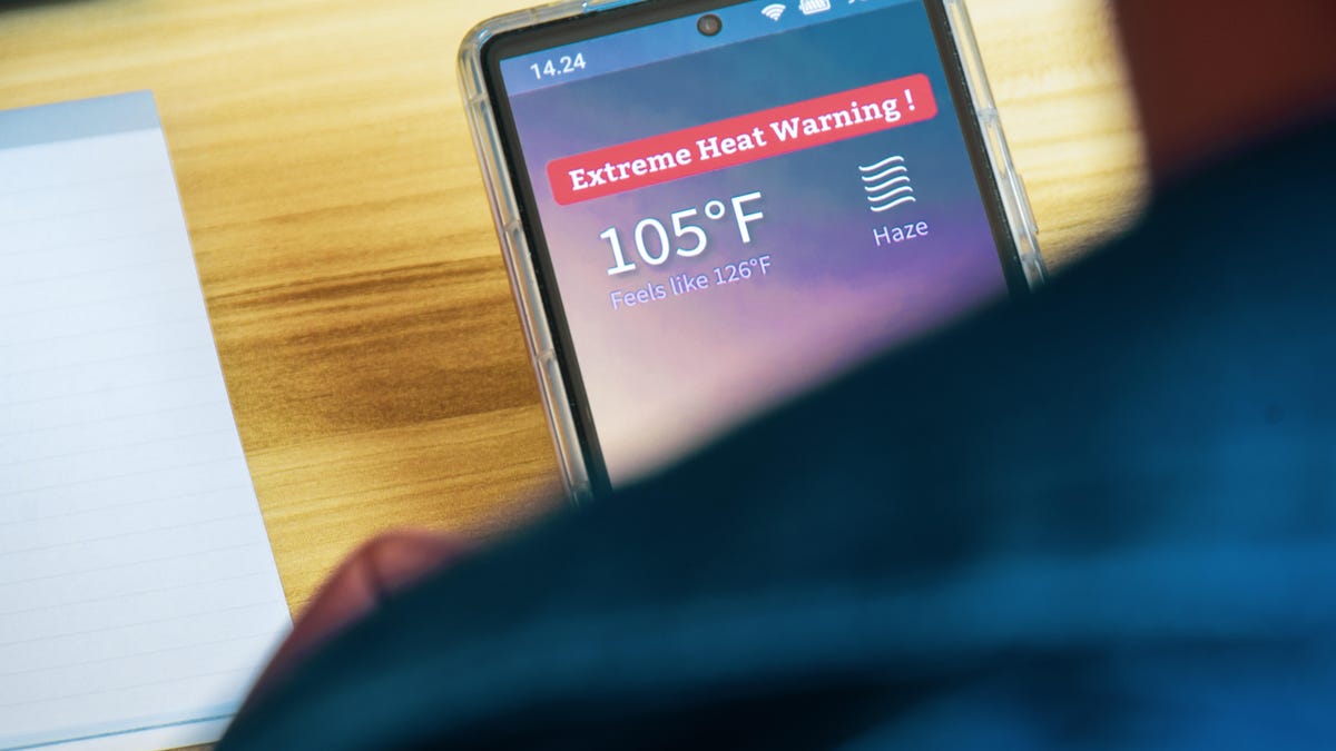 a top-down view of a smartphone over a person's shoulders. the phone says Extreme Heat Warning, 105 degrees F