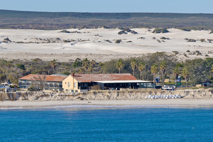 The ocean in front of a sand cliff. A building sits at the top of the sand.