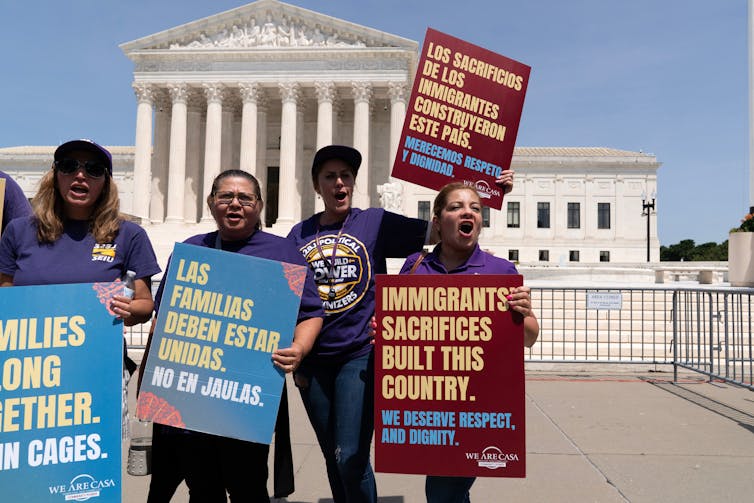 People carry signs advocating for birthright citizenship in front of an ornate stone building.