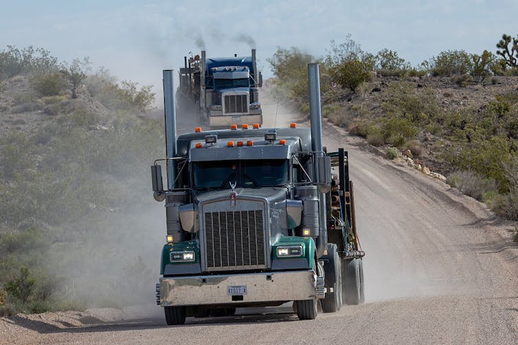 A heavy truck kicks up dust while driving on a rural road.