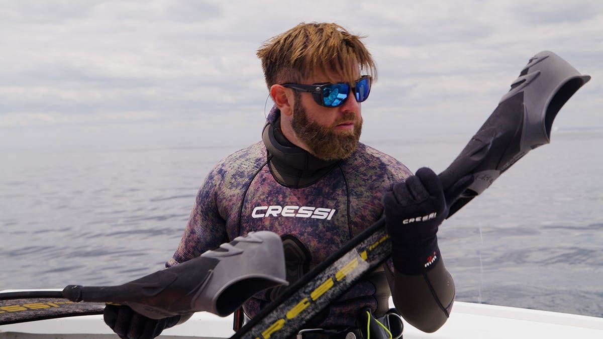 man wearing a wet suit on a boat holds his diving gear