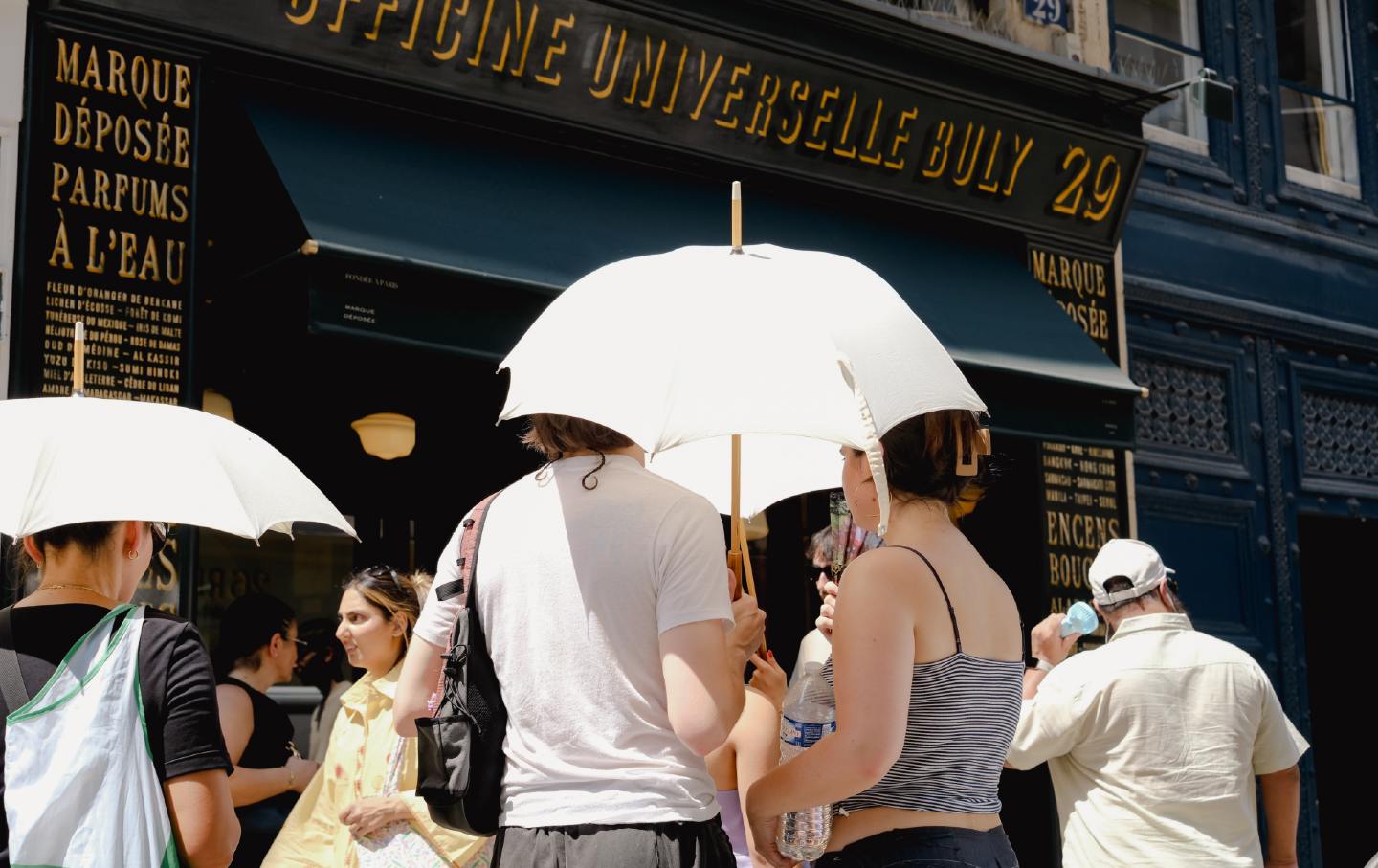 Customers queue outside a Buly shop under umbrellas to shield themselves from the heat wave in Paris, France, in July 2026.