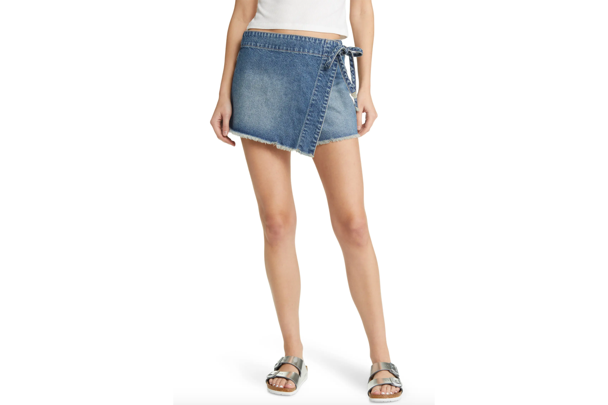 Person wearing a denim wrap skirt with a white crop top and silver sandals.