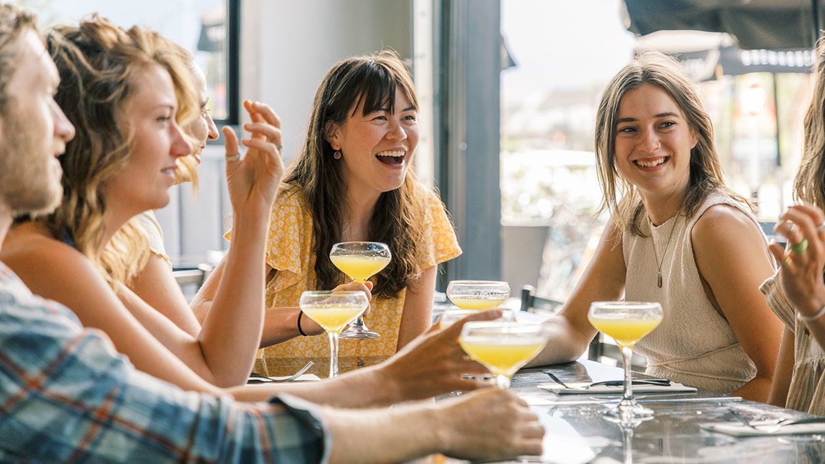 Friends drinking cocktails outside during day at restaurant.