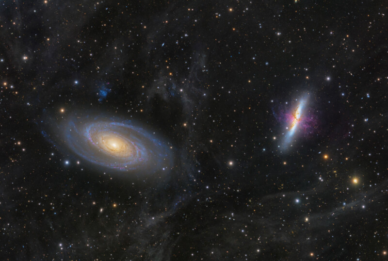 Two bright galaxies appear in a star-filled space: a spiral galaxy on the left with a glowing center and swirling arms, and an irregular, colorful galaxy on the right, both surrounded by stars and cosmic dust.