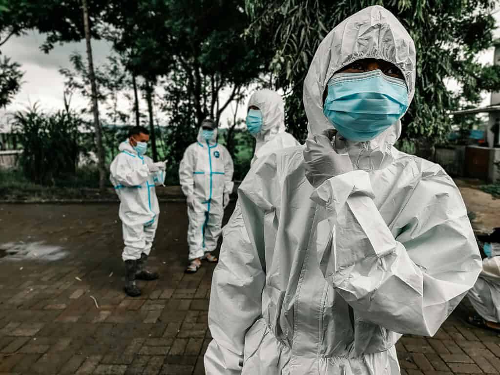 Healthcare workers wearing protective suits and masks outdoors during a health crisis.